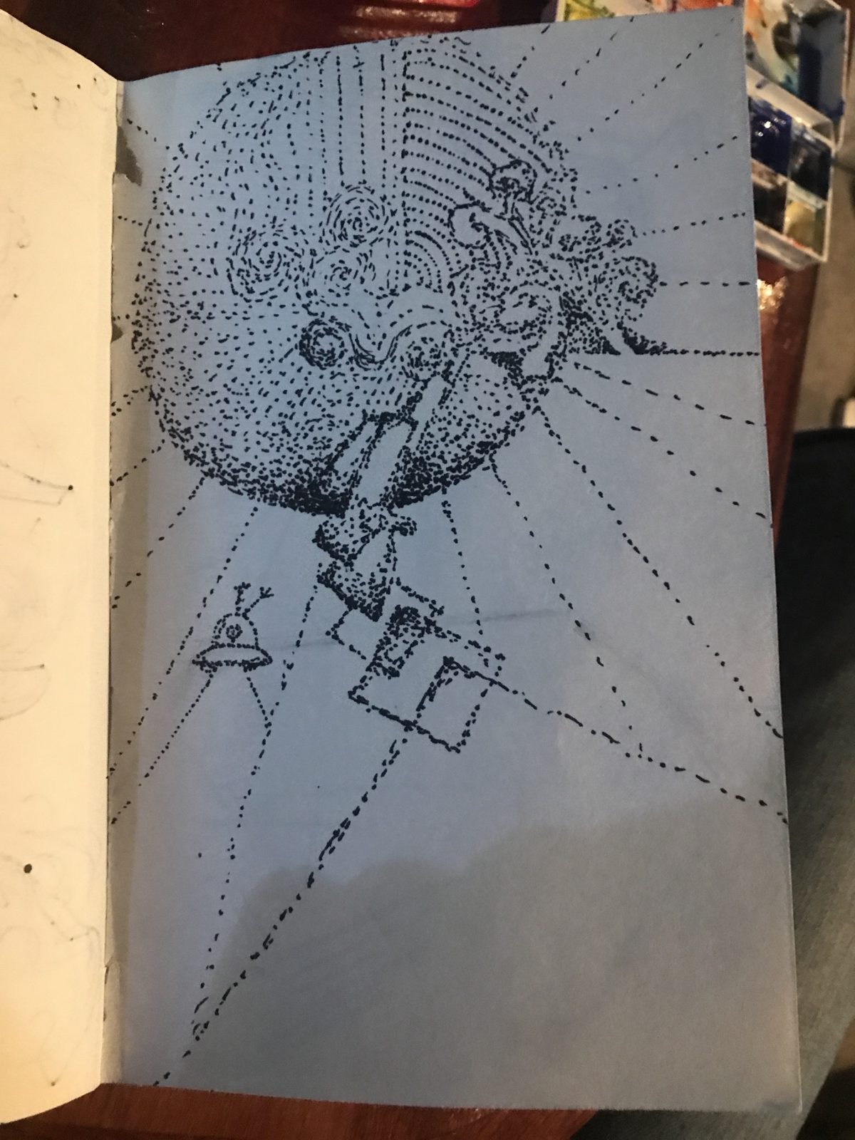 Stippled ink drawing on blue of a sphere with lines raying out and a small ufo