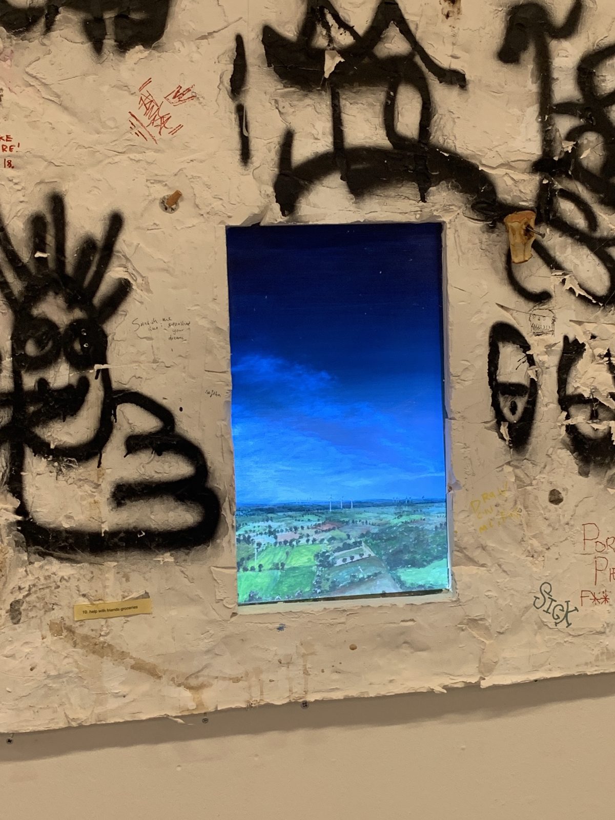 Close-up of the painting in the hole: fields and wind turbines under a dark blue sky