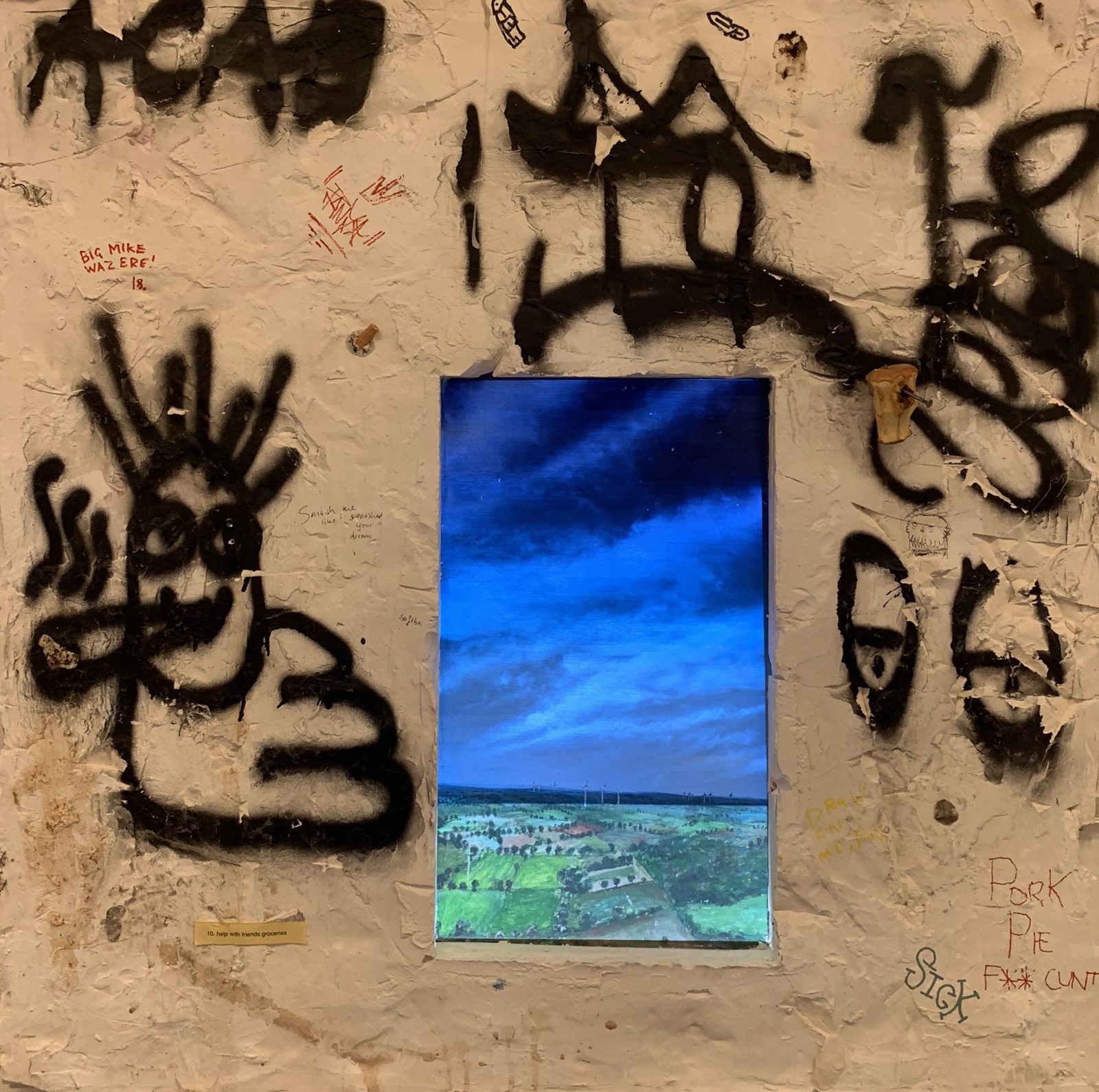 Front view: the plaster wall covered in graffiti, a painted landscape under a dark blue sky in the hole